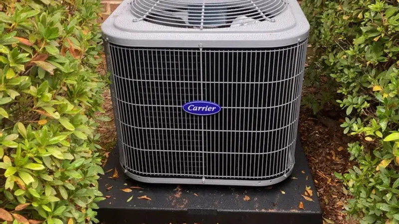 Carrier air conditioning unit installed outside a brick house with surrounding bushes and electrical connections.