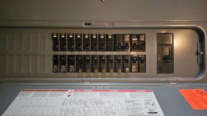 Electrical circuit breaker panel with multiple switches and safety labels inside metal enclosure.