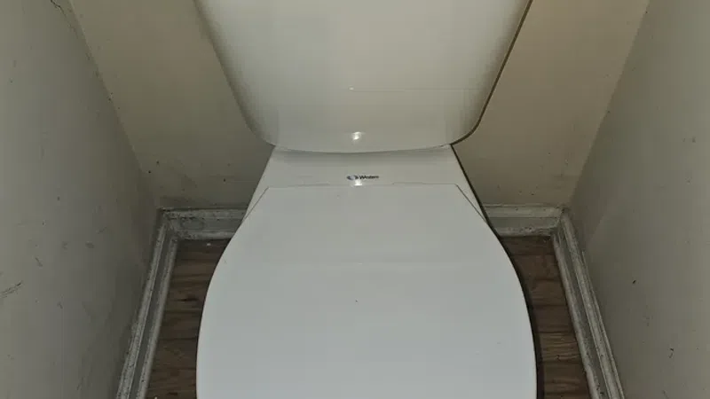 White toilet with closed lid installed against beige walls on wooden floor in small bathroom corner