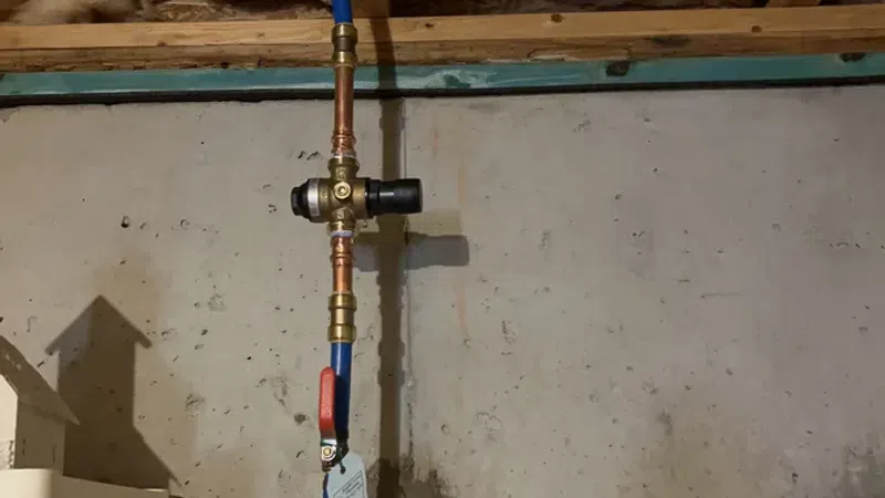 Blue PEX pipe with copper fittings and valve installed on concrete basement wall under insulation.