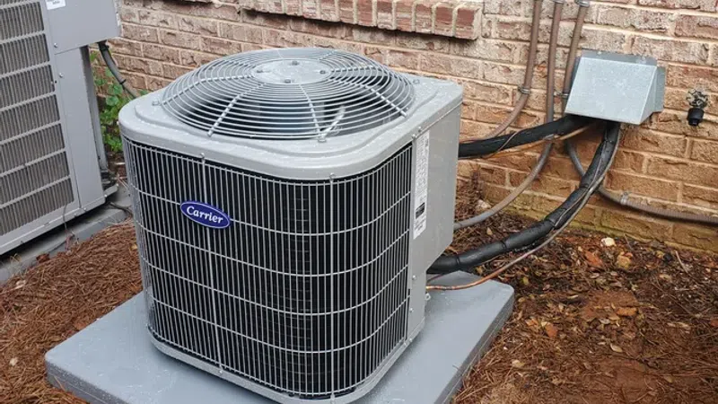 Carrier air conditioning unit installed outside a brick house on a concrete pad with electrical connections.