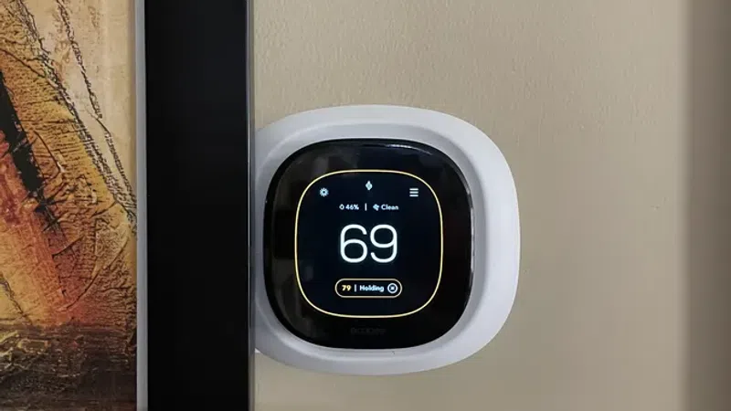 Smart thermostat mounted on beige wall next to framed abstract artwork, displaying temperature 69 degrees.