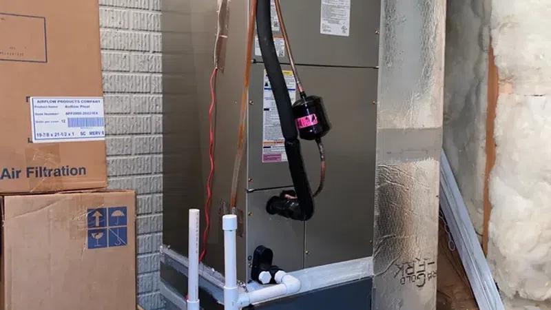 Carrier HVAC unit installation in basement with exposed insulation, cardboard boxes, and PVC plumbing pipes.