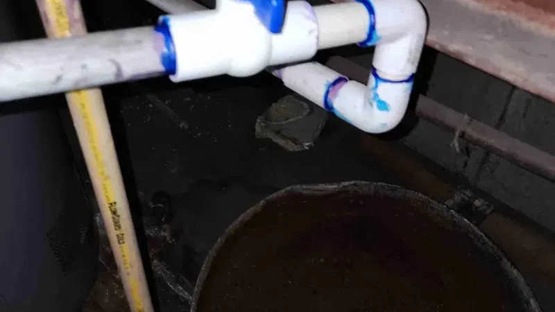 White PVC pipe with blue valve handle connected near a round container in a dimly lit industrial setting.