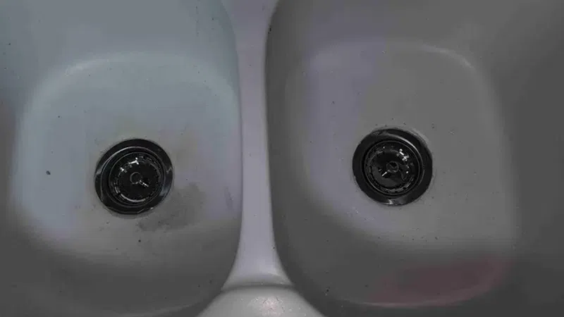 White double kitchen sink with chrome faucet and cleaning supplies around the edges.