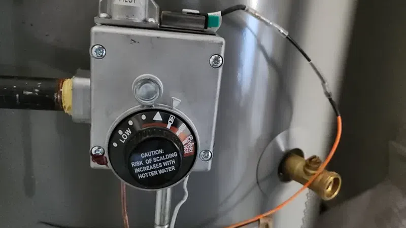 Close-up of a water heater temperature control dial with caution label and attached wiring.
