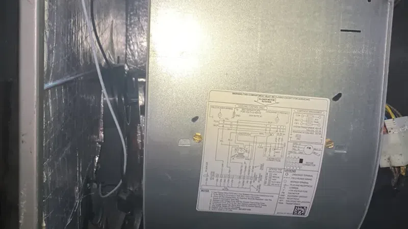 Interior view of an HVAC unit showing wiring, metal ductwork, and a system schematic label.
