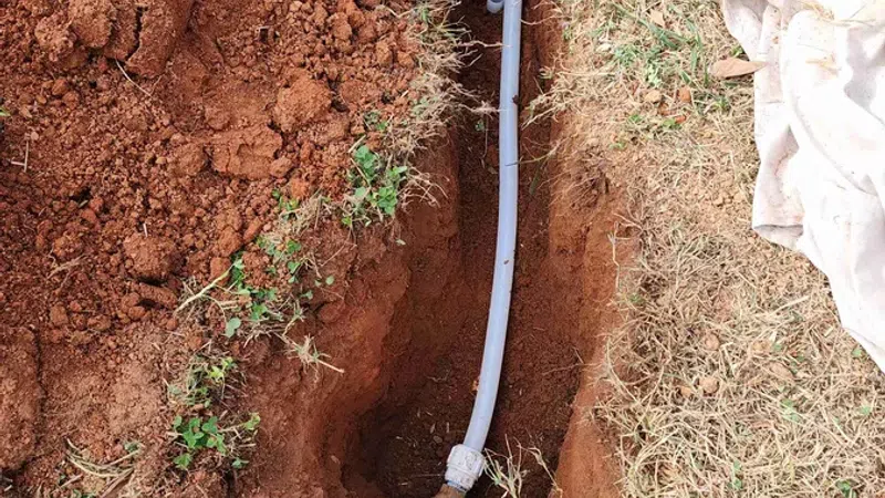 Trench dug in soil with a gray pipe installed underground and surrounding grass and dirt.