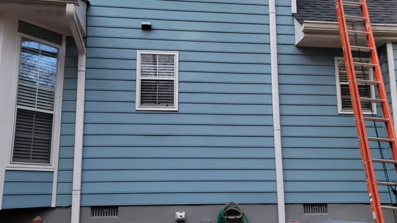 Blue two-story house exterior with white trim, windows, red ladder, wooden deck railing, and HVAC unit.