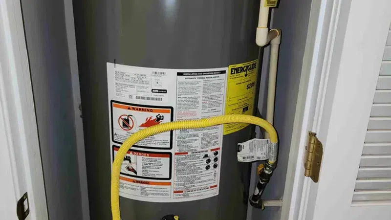 Gray Rheem water heater installed in a utility closet with yellow gas line and warning labels.