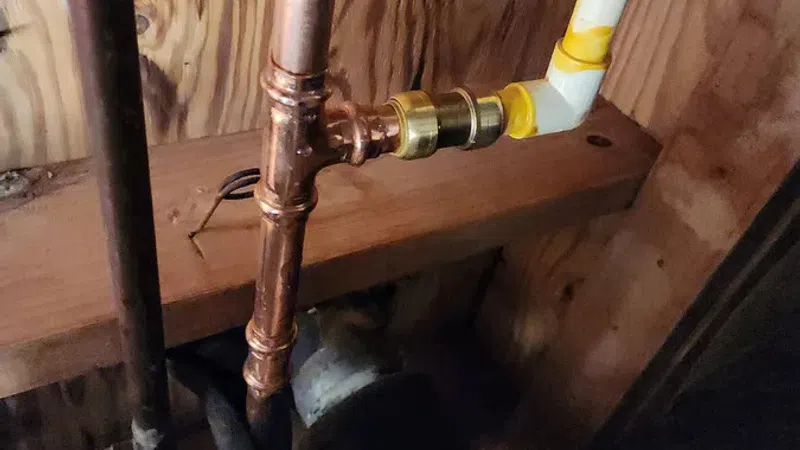 Close-up of copper and plastic plumbing pipes connected with brass fittings inside a wooden wall.
