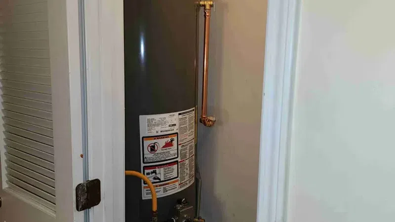 Tall Rheem water heater installed in a small utility closet with visible copper piping and vent pipe.