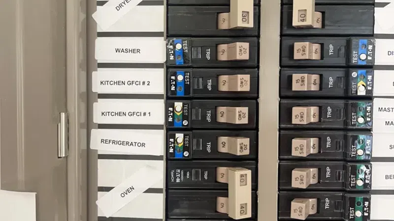 Electrical breaker panel with labeled switches for dryer, washer, kitchen appliances, and bedroom circuits.
