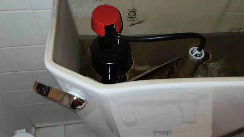 Open Glacier Bay toilet tank showing internal flushing mechanism with red and black components in bathroom.