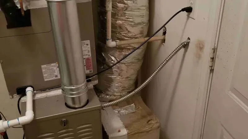 Residential heating furnace with ductwork and insulation installed in a utility room near a closed door.