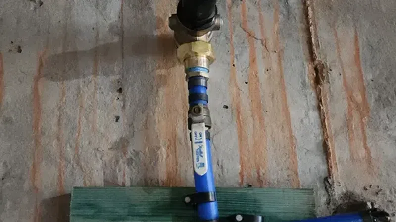 Blue PVC pipes with valves and fittings mounted on a rough concrete wall and wooden supports for plumbing.