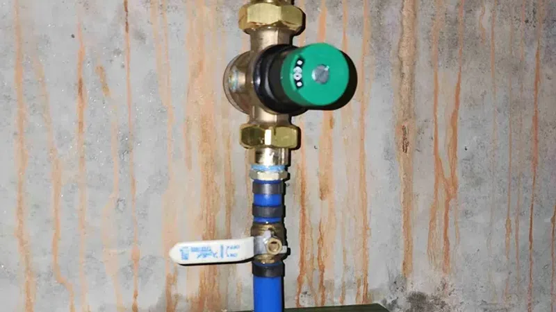 Blue water pipes with brass valve and green dial mounted on a stained concrete wall with wooden support.
