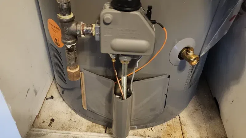 Close-up of a residential gas water heater with visible pipes, warning labels, and control valve.