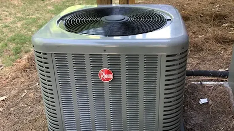Outdoor Rheem air conditioning unit installed on a concrete pad in a backyard with grass and wooden structures.