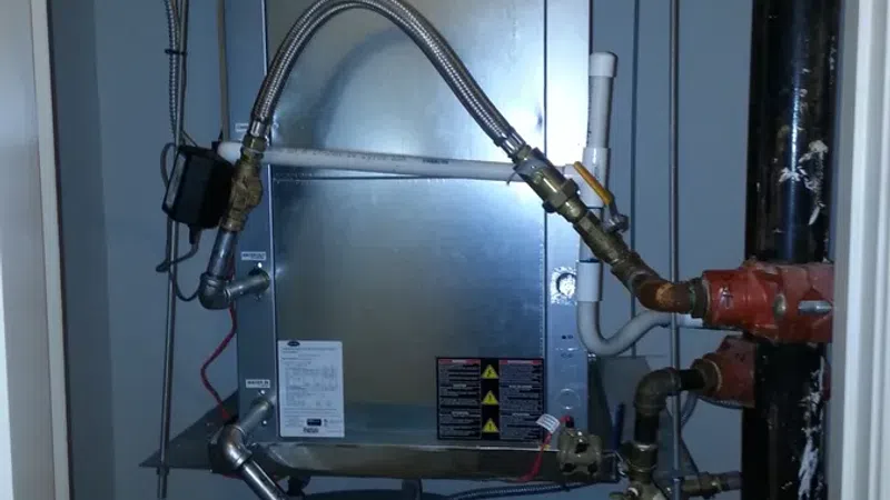 Carrier HVAC unit and water heater connected by metal and plastic pipes in a utility closet.