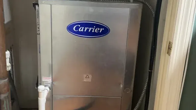 Carrier HVAC unit with connected black hoses and insulated ducting installed in a home utility closet.