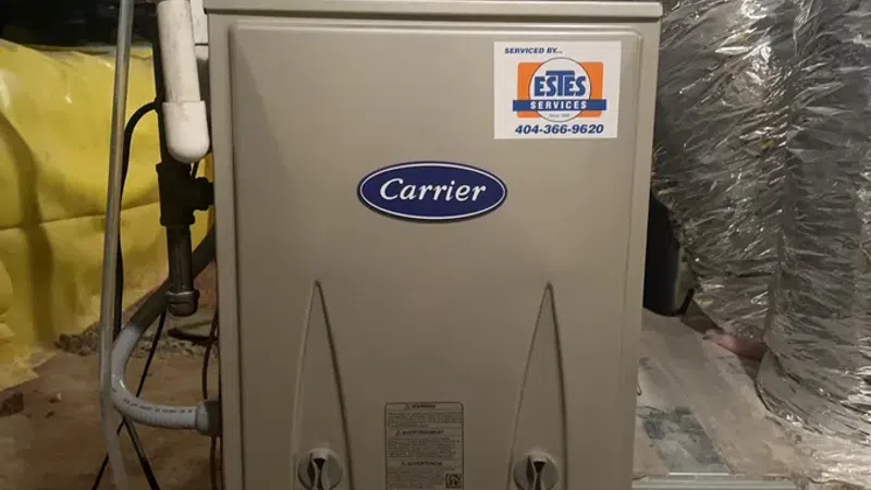 Carrier HVAC furnace unit installed in a basement with visible piping and Estes Services sticker.