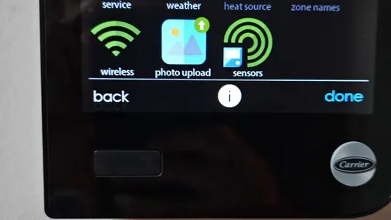 Smart thermostat screen displaying service, weather, wireless, photo upload, sensors, and heat source icons.
