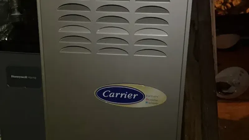 Gray Carrier furnace with vents installed in a basement or utility space with visible pipes and ducts.