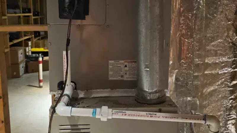 Basement furnace unit with pipes and ductwork in an insulated utility room with exposed wooden shelving.