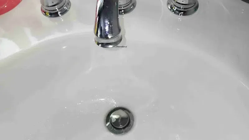 Clean white bathroom sink with shiny chrome faucet and handles under bright lighting.
