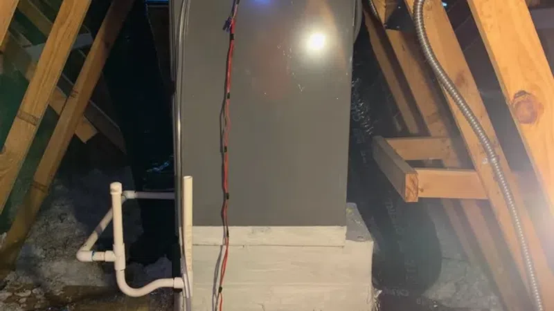 Attic HVAC system with insulated ductwork, wooden beams, and electrical wiring inside a house attic space.