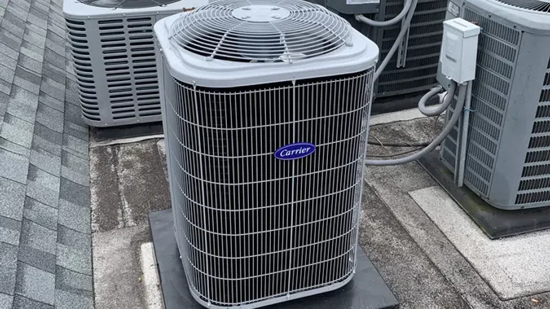 Multiple rooftop air conditioning units including Carrier brand on asphalt roof with shingle edge under overcast sky