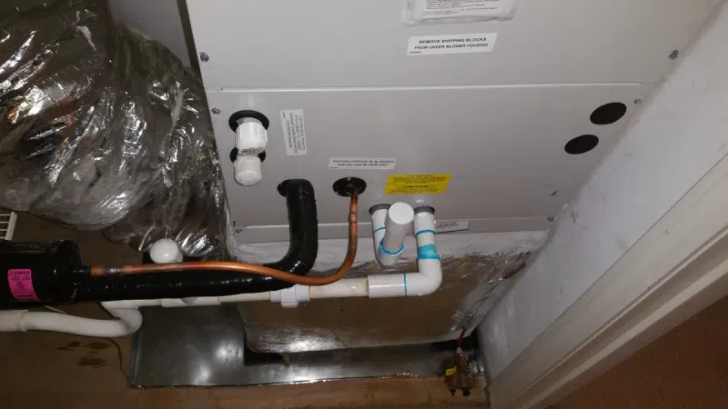 Indoor HVAC unit with connected copper and PVC pipes for heating and cooling system operation.