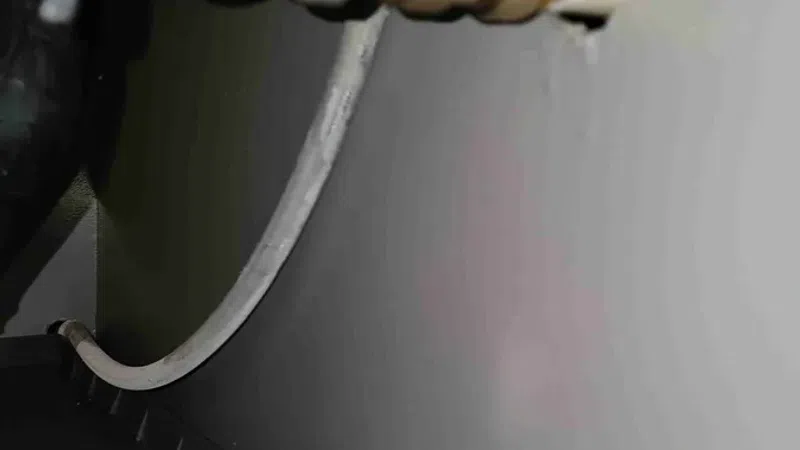 Close-up of a metal plumbing pipe connected through a hole in a wall with a white cable looped below.