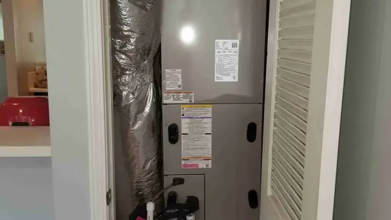 Carrier HVAC unit installed in a small closet with insulated ductwork and white louvered doors.