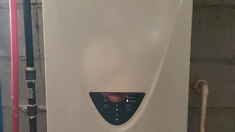 AO Smith water heater with connected pipes mounted on a concrete block wall in utility space.
