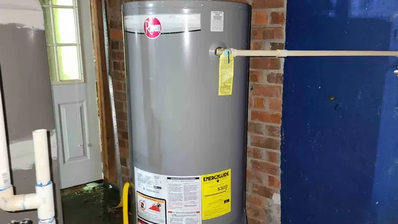 Gray Rheem water heater with energy guide label installed in a basement with brick wall and blue painted section.