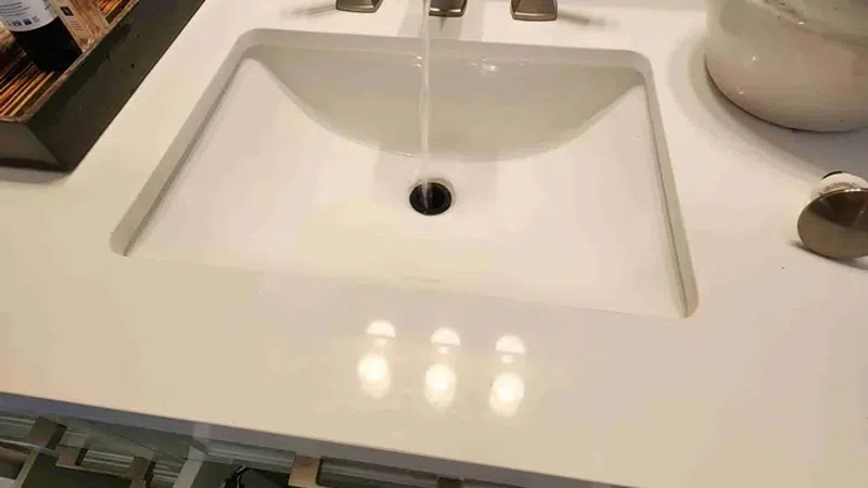 Modern bathroom sink with water running from a sleek faucet, surrounded by toiletries and decorative vase.