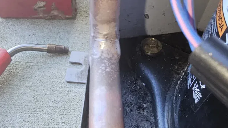 Close-up of a copper pipe showing soldering joint near HVAC components and colored electrical wires.