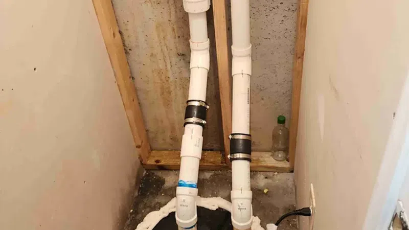 Basement sump pump installation with white PVC pipes and foam sealant around the pump cover in a concrete floor.