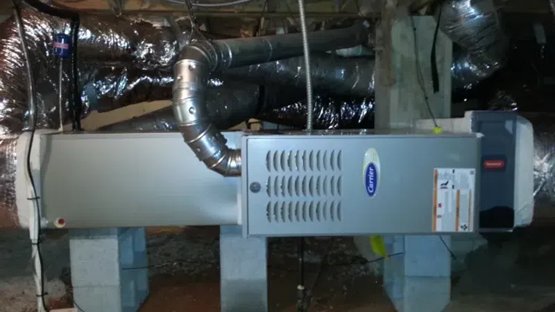 Carrier furnace unit installed in a basement with ductwork and insulation around it