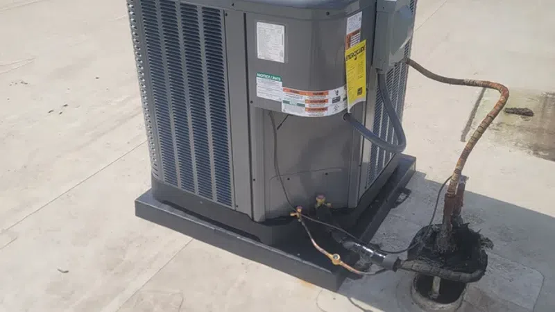 Commercial rooftop HVAC unit with fan and connected copper piping under clear sky on flat roof.