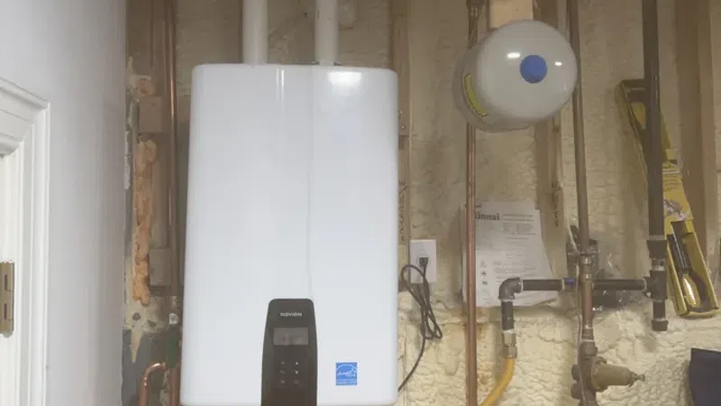 Modern tankless water heater installed in a utility room with exposed pipes and insulation walls.