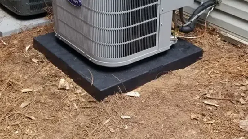 Two outdoor HVAC units installed outside a house on a bed of pine straw and dirt.