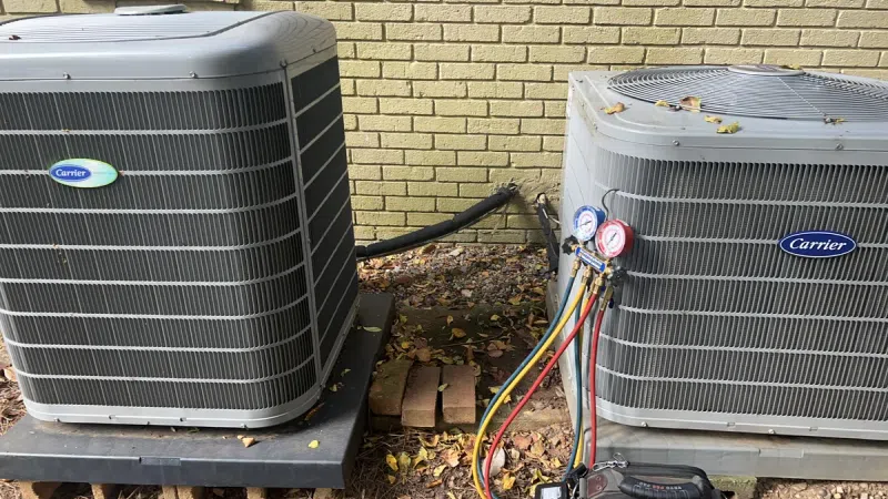 Two outdoor Carrier HVAC units installed side by side on concrete pads beside a brick wall with service gauges attached
