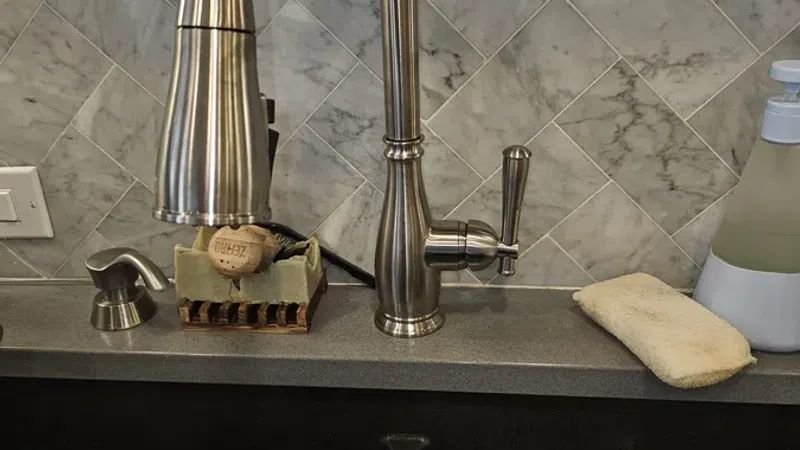 Modern kitchen sink area with brushed metal faucet, marble tile backsplash, soap dispenser, and cleaning sponge.