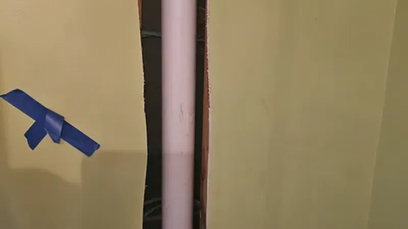 Exposed vertical white pipe installed inside a wall cavity with cut drywall and construction tools nearby.