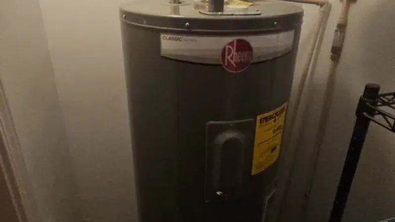 Rheem Classic Series water heater connected to copper and PVC pipes in a utility room.
