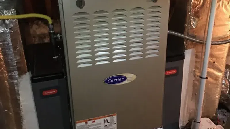 Carrier brand furnace installed in an attic with vent pipes and insulation around the unit.
