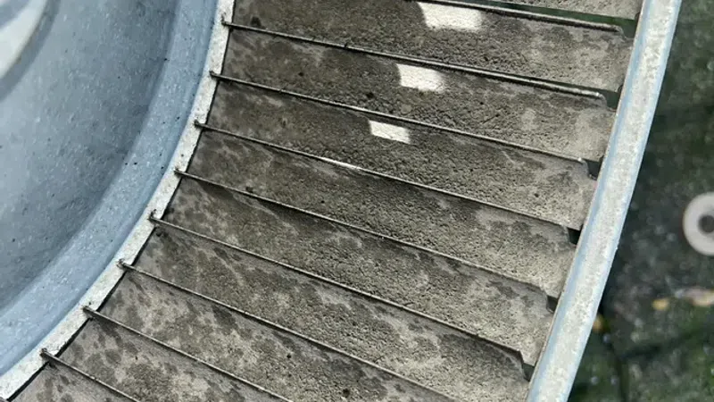 Close-up of a dusty, weathered metal fan blade inside a circular housing outdoors.